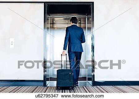 Stock Photo - Businessman with wheeled luggage entering hotel lift. Fotosearch