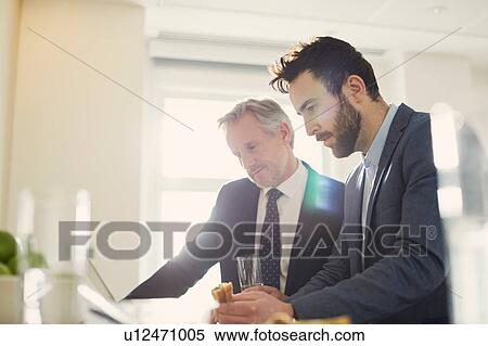 Businessmen looking at laptop over working lunch View Large Photo Image Stock Photography - Businessmen looking at laptop over working lunch. Fotosearch