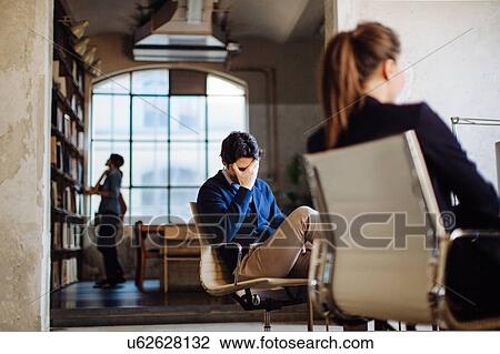 Stock Image - Businesspeople in office, businessman sitting in chair, head in hands. Fotosearch