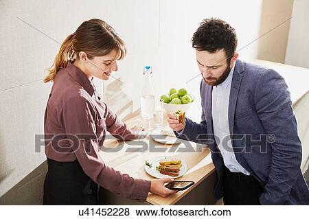 Stock Photo - Businesswoman and man looking at smartphone during working lunch. Fotosearch