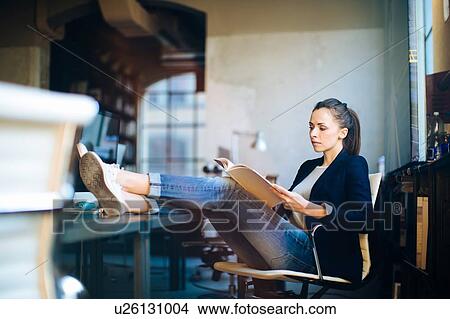 Businesswoman sitting at desk, feet up on desk, looking at documents View Large Photo Image Picture - Businesswoman sitting at desk, feet up on desk, looking at documents. Fotosearch