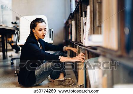 Stock Photo - Businesswoman sitting on office floor, looking through filing cabinet. Fotosearch