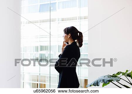 Businesswoman using mobile phone by window View Large Photo Image Stock Photograph - Businesswoman using mobile phone by window. Fotosearch