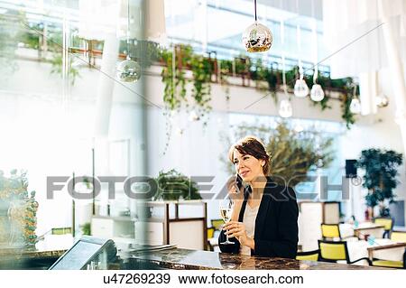 Stock Photo - Businesswoman using mobile phone while having drink at bar. Fotosearch
