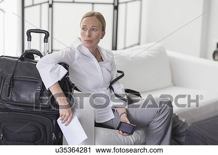 Stock Image - Businesswoman waiting with suitcase in hotel lobby. Fotosearch