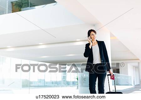 Stock Image - Businesswoman with wheeled luggage in hotel building. Fotosearch