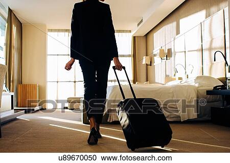 Stock Image - Businesswoman with wheeled luggage in hotel bedroom. Fotosearch