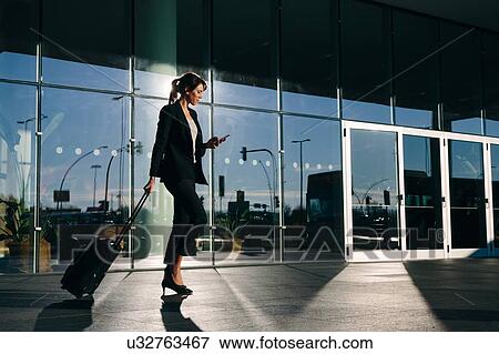 Businesswoman with wheeled luggage passing glass building, Malpensa, Milan View Large Photo Image Stock Photo - Businesswoman with wheeled luggage passing glass building, Malpensa, Milan. Fotosearch