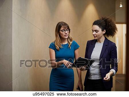 Businesswomen walking and looking at digital tablet in office corridor View Large Photo Image Stock Photography - Businesswomen walking and looking at digital tablet in office corridor. Fotosearch
