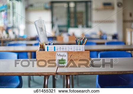 Stock Image - Classroom desk with wooden box full of pencils and rulers in primary school classroom. Fotosearch