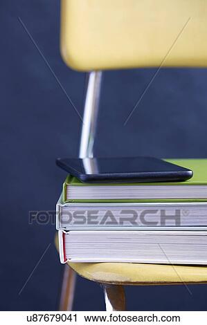 Stock Image - Close up of tablet and books on chair. Fotosearch