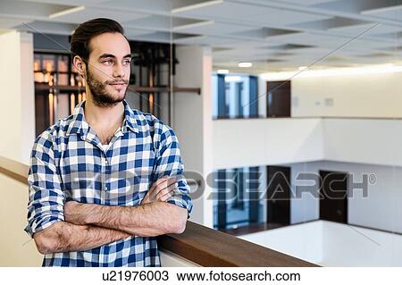 Stock Image - Confident young businessman looking out over office atrium. Fotosearch