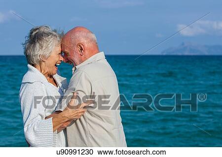 Stock Image - Couple hugging and laughing by seaside. Fotosearch