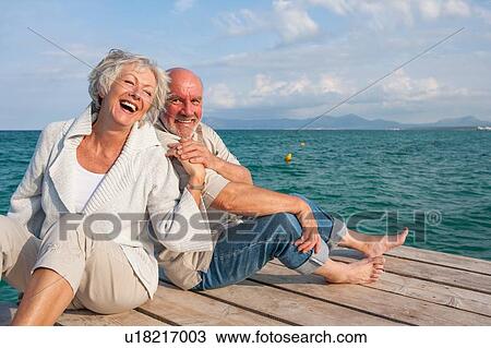 Stock Image - Couple hugging and laughing on jetty. Fotosearch