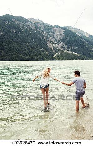 Stock Image - Couple in shallow water holding hands, Achensee, Innsbruck, Tirol, Austria, Europe. Fotosearch