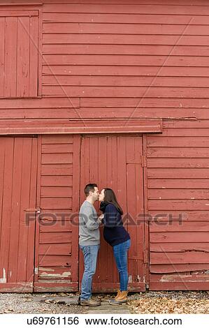 Stock Photograph - Couple kissing in front of red barn. Fotosearch