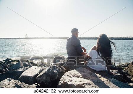 Couple sitting on coastal rocks, looking at view, rear view View Large Photo Image Stock Image - Couple sitting on coastal rocks, looking at view, rear view. Fotosearch