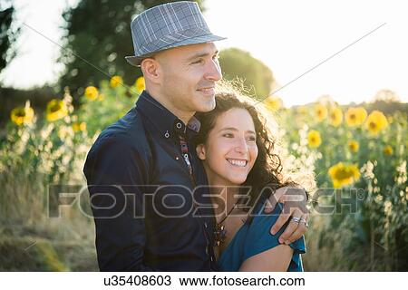 Stock Image - Couple standing in field of sunflowers, hugging. Fotosearch