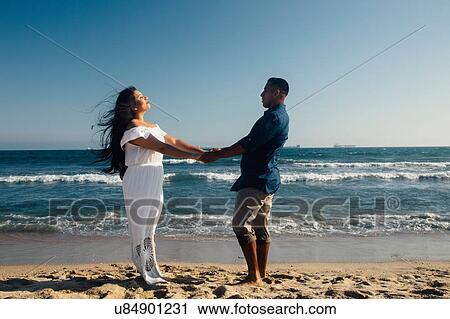 Stock Image - Couple standing on beach, holding hands, face to face, Seal Beach, California, USA. Fotosearch