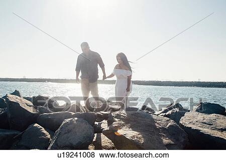 Stock Photo - Couple walking on coastal rocks, holding hands, Seal Beach, California, USA. Fotosearch