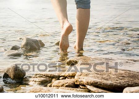 Stock Image - Cropped view of woman barefoot in water. Fotosearch