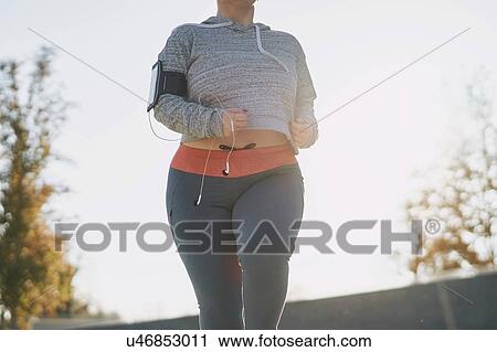 Stock Image - Curvaceous young female runner running in park, mid section. Fotosearch