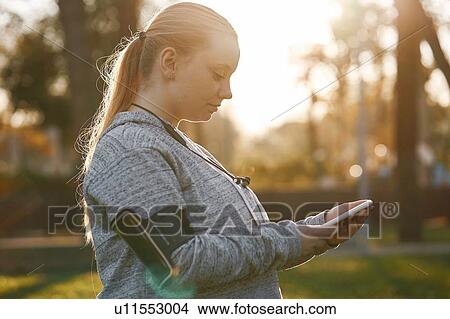 Curvaceous young woman training in park, looking at smartphone View Large Photo Image Picture - Curvaceous young woman training in park, looking at smartphone. Fotosearch