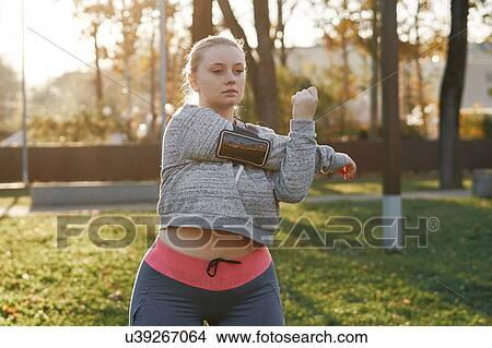 Picture - Curvaceous young woman training in park, stretching arms. Fotosearch