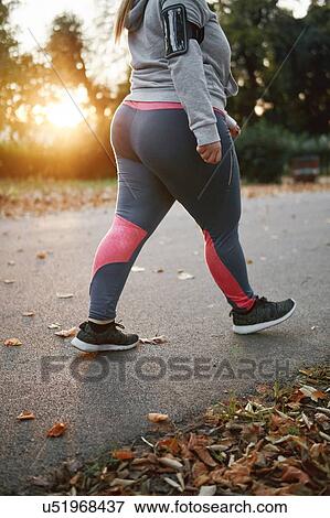 Stock Photo - Curvaceous young woman training, neck down view walking in park. Fotosearch