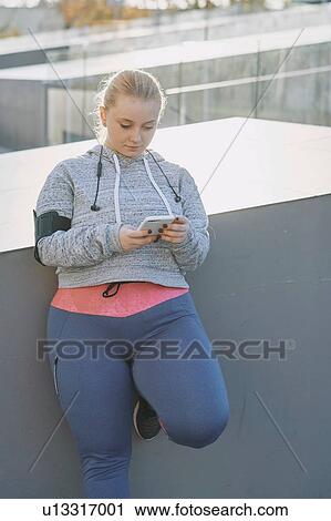 Curvaceous young woman training, leaning against wall looking at smartphone View Large Photo Image Stock Image - Curvaceous young woman training, leaning against wall looking at smartphone. Fotosearch