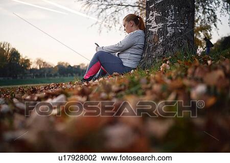 Stock Image - Curvaceous young woman training, taking a break looking at smartphone in park. Fotosearch