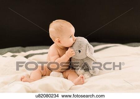 Cute baby girl sitting up on bed with soft toy View Large Photo Image Picture - Cute baby girl sitting up on bed with soft toy. Fotosearch