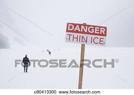 Stock Image - Danger sign and people on frozen Lake Louise, Canada. Fotosearch