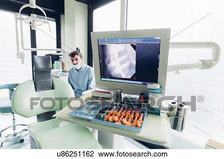 Stock Image - Dental x-ray on computer screen, dentist in background. Fotosearch