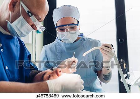 Dentist and dental nurse carrying out dental procedure on male patient, close-up View Large Photo Image Stock Photo - Dentist and dental nurse carrying out dental procedure on male patient, close-up. Fotosearch