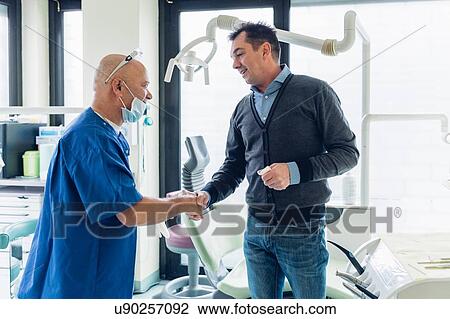 Stock Image - Dentist and male patient in dentist office, shaking hands. Fotosearch