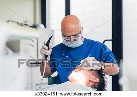 Stock Image - Dentist carrying out dental procedure on male patient. Fotosearch