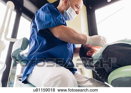 Dentist carrying out dental procedure on male patient View Large Photo Image Stock Photo - Dentist carrying out dental procedure on male patient. Fotosearch