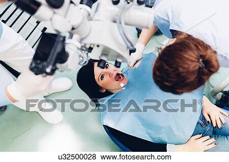 Stock Photo - Dentist carrying out procedure on female patient, elevated view. Fotosearch
