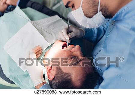 Stock Photo - Dentist looking into male patient's mouth, elevated view. Fotosearch