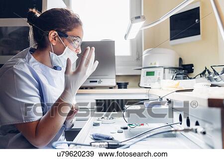 Stock Photo - Dentist putting on surgical gloves, preparing to use dentistry equipment. Fotosearch
