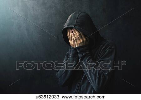 Stock Image - Desperate man in hooded jacket crying.. Fotosearch