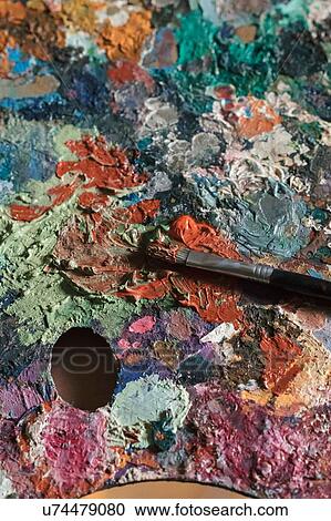Stock Image - Detail of messy artist palette and paintbrush in artists studio, close up. Fotosearch