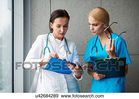 Stock Photo - Doctor and surgeon talking in hallway, looking at clipboard. Fotosearch