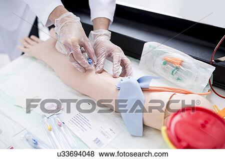 Stock Photo - Doctor practising inserting an IV (intravenous) line on a training dummy.. Fotosearch