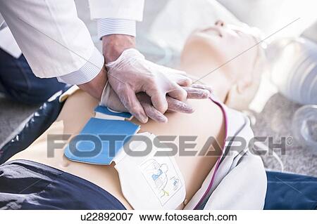 Stock Photo - Doctor undertaking CPR training on dummies. Automated external defibrillator pads have been placed on the dummy's chest.. Fotosearch