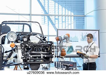 Stock Photograph - Engineer and robot assembling car in robotics research facility. Fotosearch