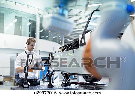 Stock Photograph - Engineer and robot inspecting car in robotics research facility. Fotosearch