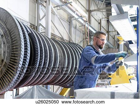 Stock Image - Engineer at workstation with high pressure steam turbine in turbine maintenance factory. Fotosearch