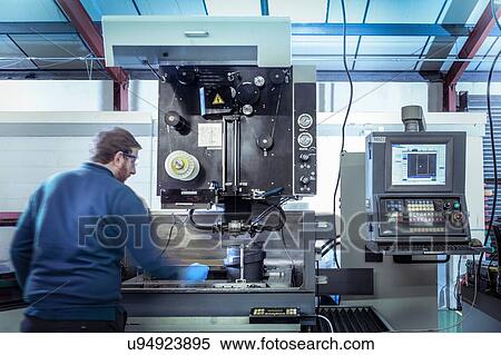 Stock Photography - Engineer operating a wire erosion machine in precision engineering factory. Fotosearch